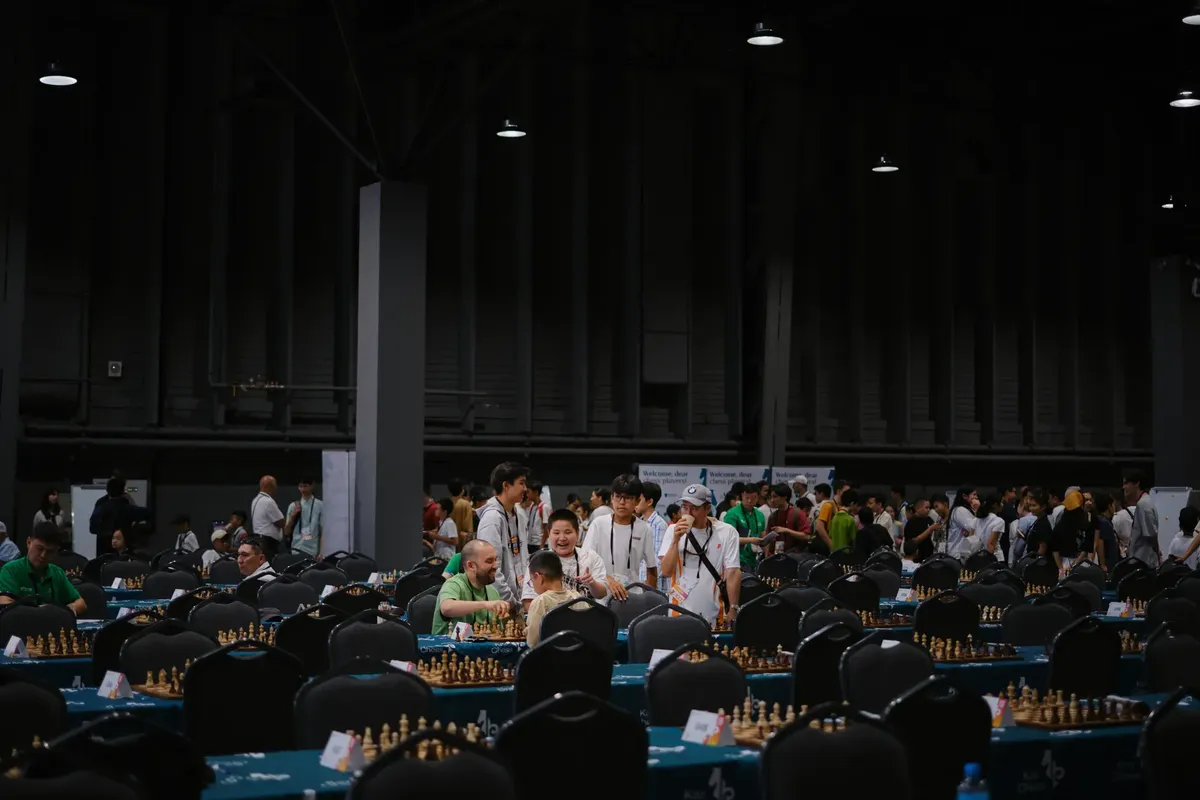 屋内でのチェス tournament で、多様な参加者がテーブルの周囲に集まります。