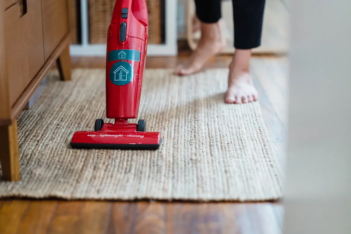A red vacuum cleaner on a carpet in a stylish home setting with barefoot user.